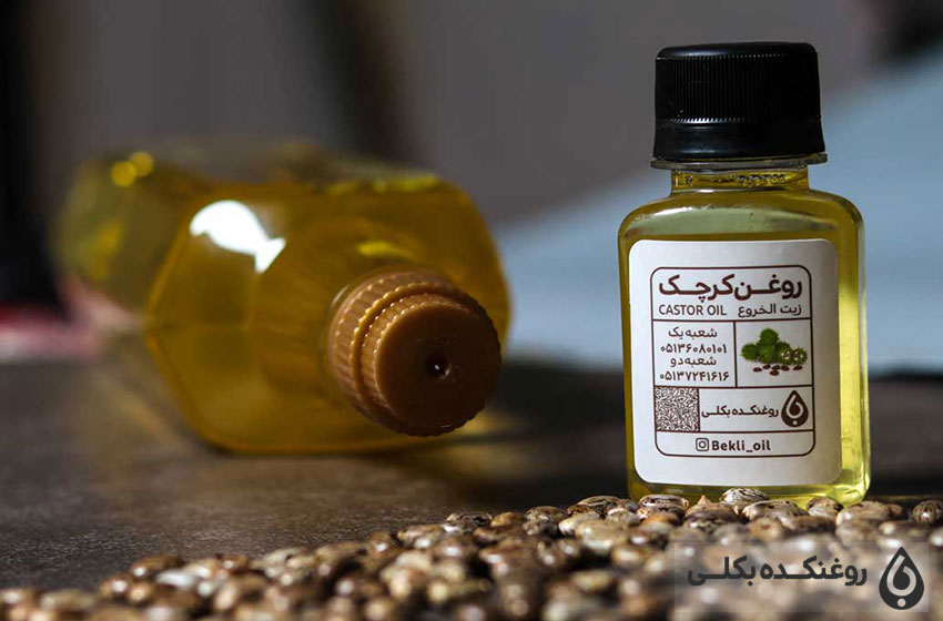 یک شیشه حاوی روغن کرچک به همراه یک بطری روغن و دانه های کرچک
