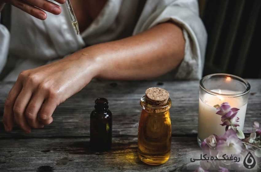 دو شیشه حاوی روغن خراطین و شمع و شاخه گل و مردی درحال ریختن خراطین روی پوست خودش