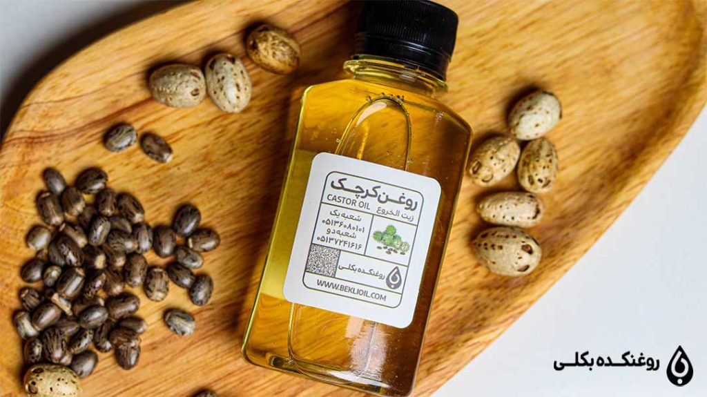 یک شیشه روغن کرچک و چند دانه کرچک روی یک تخته چوبی