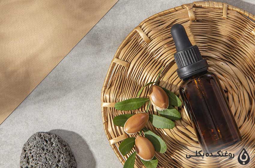 یک شیشه روغن آرگان بر روی یک ظرف به همراه یک سنگ و دانه های آرگان
