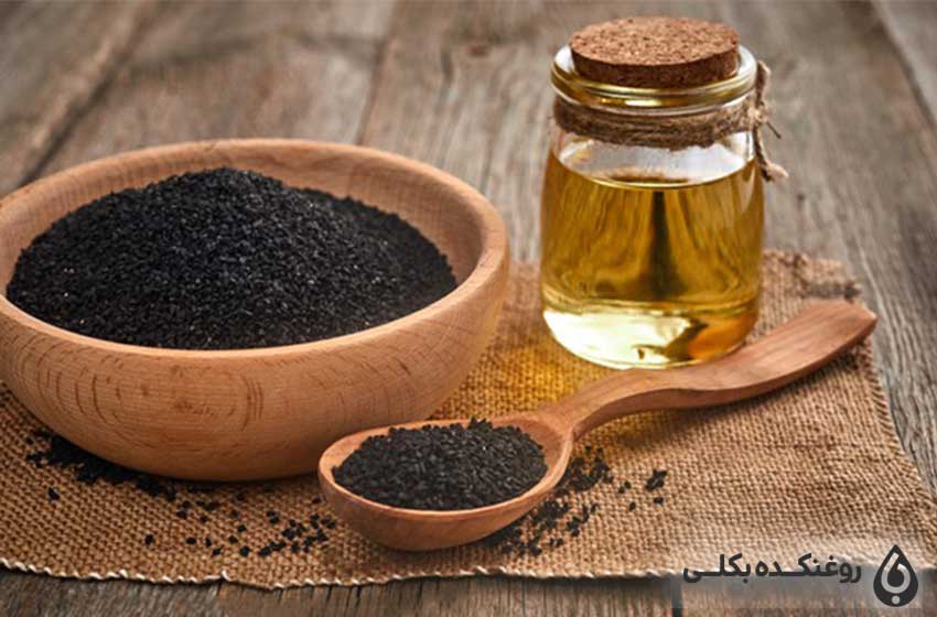 یک شیشه حاوی روغن سیاه دانه به همراه یک ظرف و یک قاشق با دانه های سیاه دانه