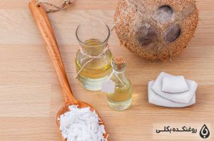 دو شیشه حاوی روغن نارگیل به همراه یک نارگیل و یک قاشق دارای تکه های نارگیل