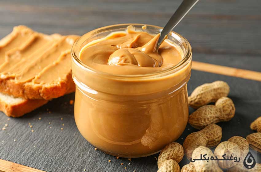 یک شیشه حاوی کره بادام زمینی و دانه های بادام زمینی به همراه یک نان تست