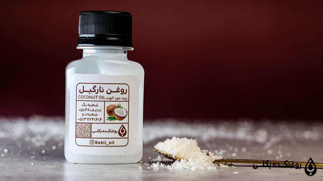 یک شیشه روغن نارگیل در کنار یک قاشق پودر نارگیل
