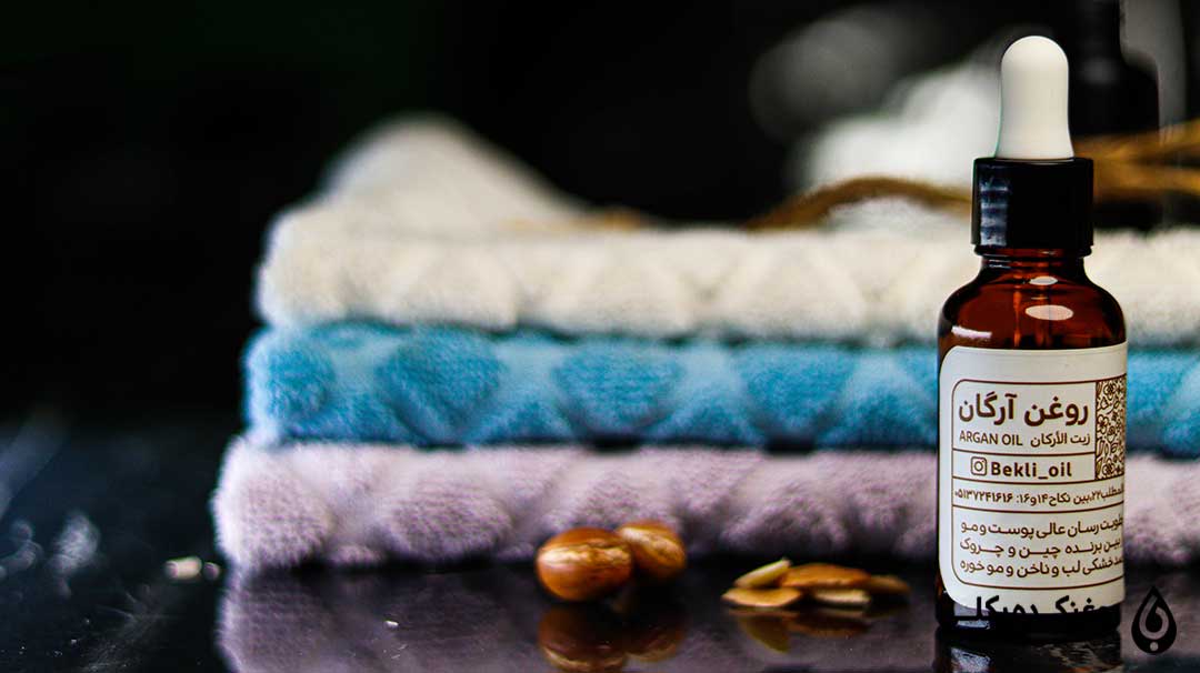 روغن آرگان در کنار دانه آرگان و تعدادی حوله